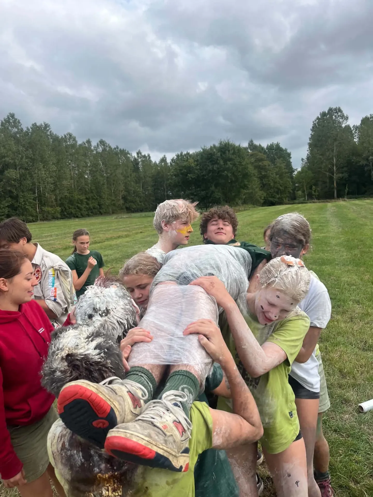 Scouts dragen een ingepakte deelnemer door de lucht tijdens een spel